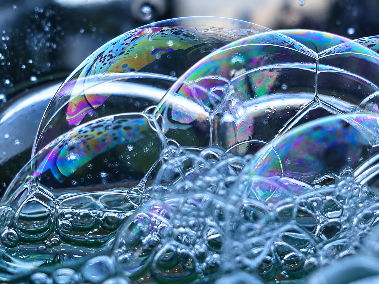 Gros plan macro de bulles de savon transparentes aux reflets irisés violets, verts et bleus, empilées dans la mousse.